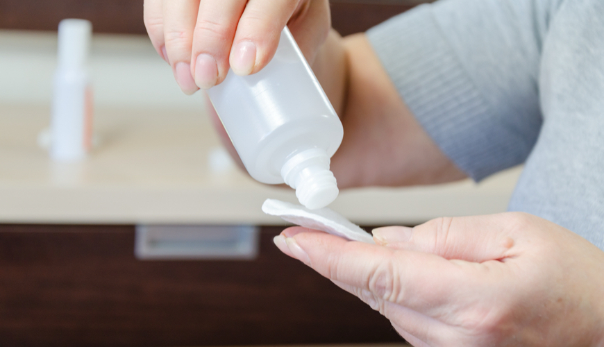 Close-up of hands applying rubbing alcohol to a cotton pad for removing sticker residue.