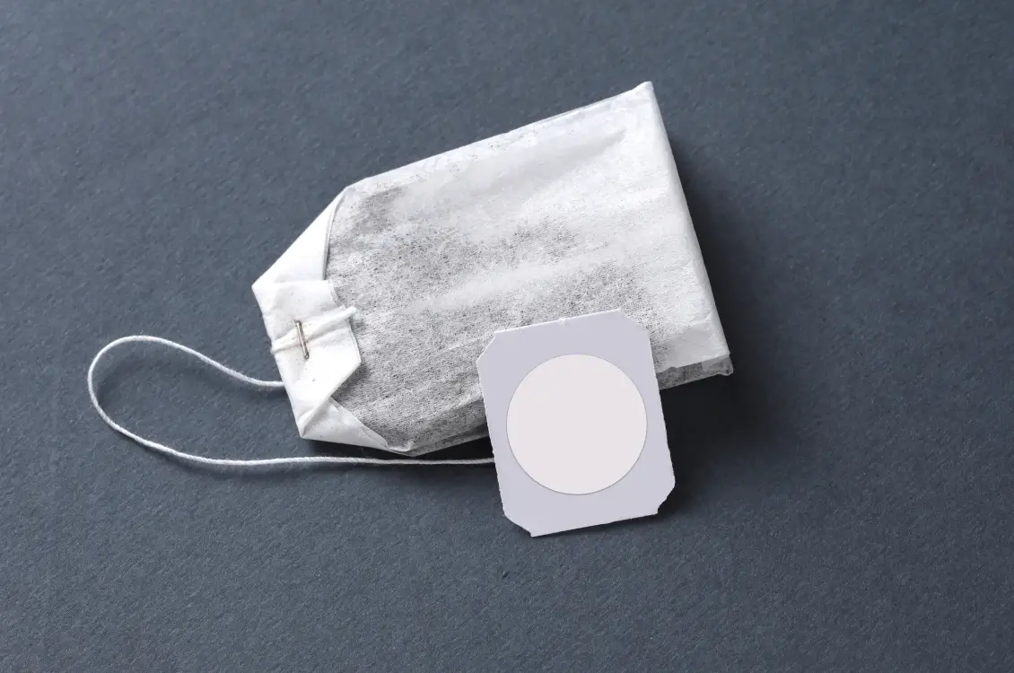 Tea bag with a blank round, white label on its tag against a dark gray background.