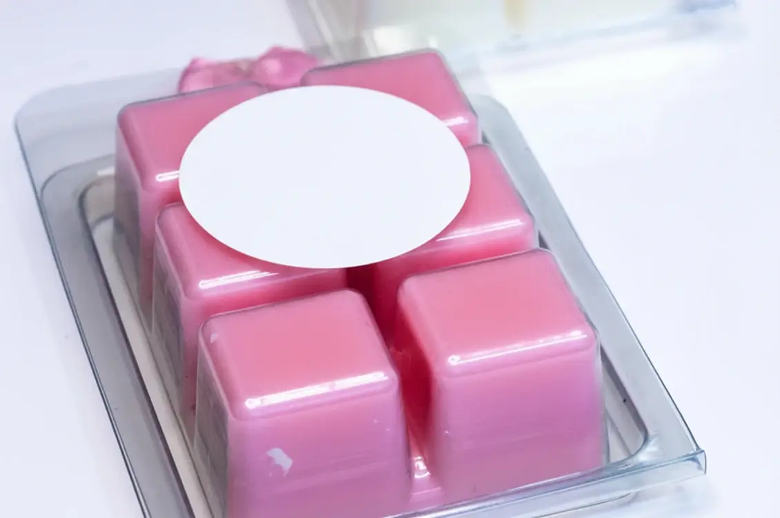 Pink wax melt cubes in a clear clamshell package with a round blank white label on top.